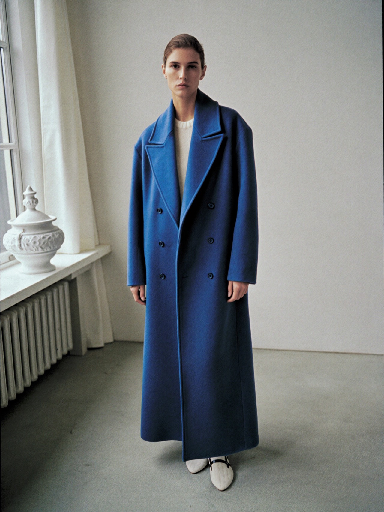 Woman in a long cobalt wool coat against a porcelain studio wall