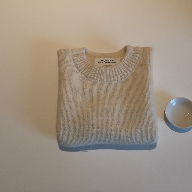 Folded ecru cable knit sweater beside a small ceramic dish