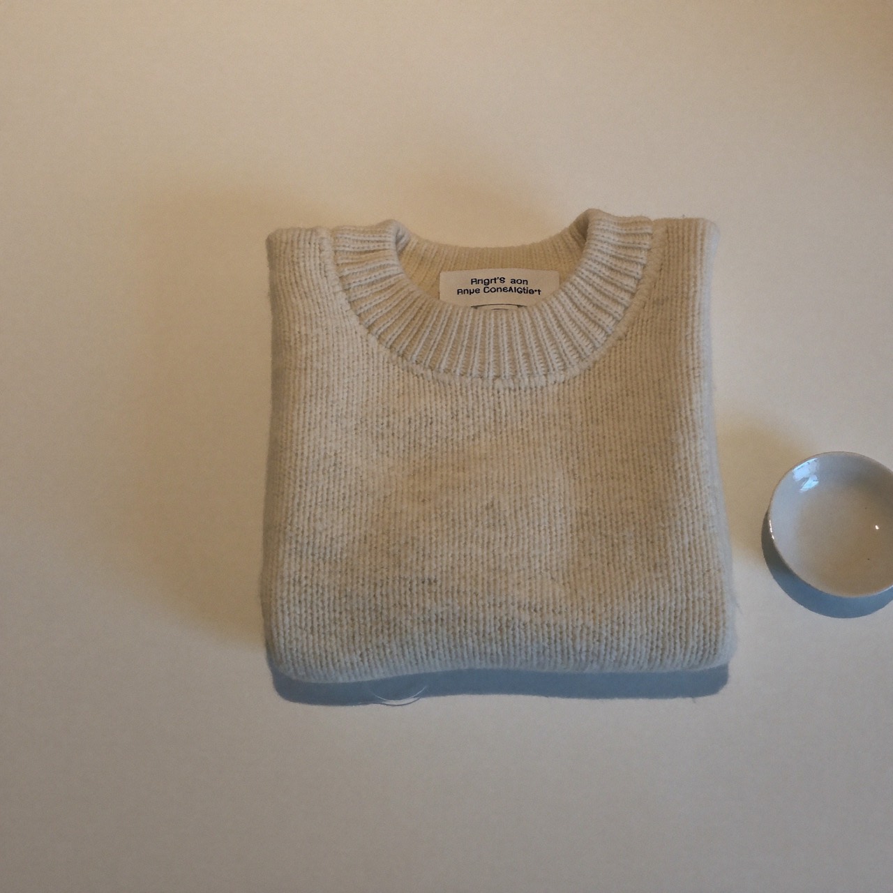 Ecru cable knit sweater folded beside a small ceramic dish on porcelain linen